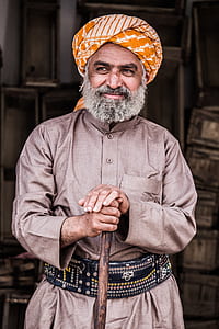 man in gray dress shirt and white and orange kiffeyeh holding brown walking cane thumbnail