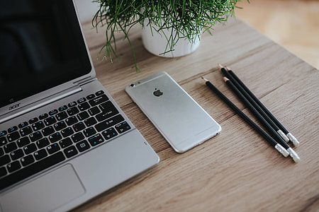 Silver Acer laptop on a wooden desk with a green plant, pencils and an Apple iPhone thumbnail