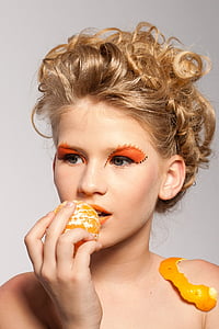 woman with orange eyeshadow holding peeled orange fruit thumbnail