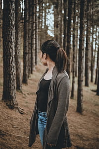 woman standing near brown trees looking behind during daytime thumbnail