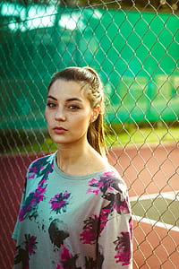 woman wearing multicolored floral shirt standing beside gray metal fence during daytime thumbnail