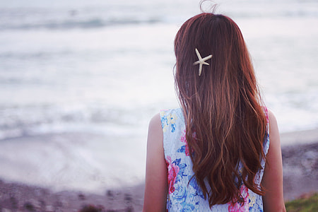 girl wearing white floral-pattern sleeveless shirt and starfish hairclip facing backwards near beach at daytime thumbnail