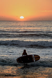 silhoutte photo of a person towards sea wave holding surfing board during golden hour thumbnail