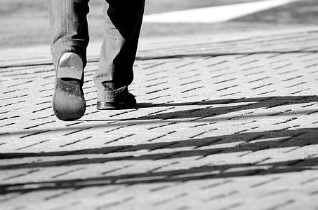person wearing pair of black shoes while walking on gray pavement thumbnail