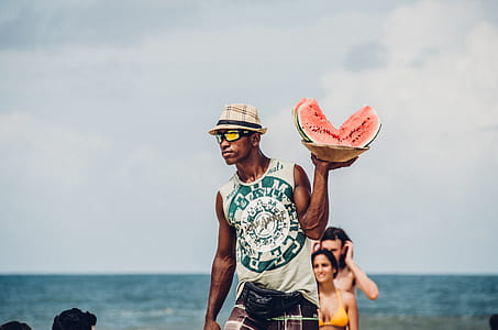 selective focus photography of man carrying a plate of sliced watermelons on shore at daytime thumbnail