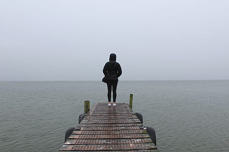 person standing on brown dock staring at horizon thumbnail