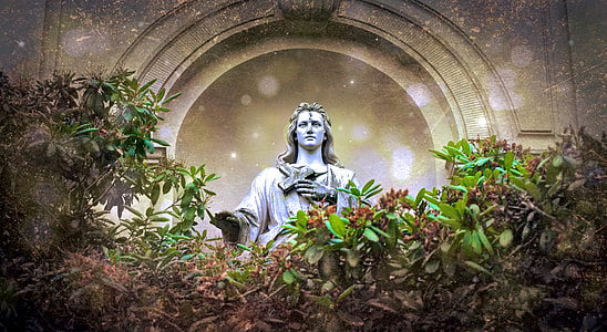 Concrete statue holding cross surrounded by green leaves thumbnail