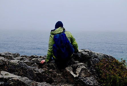 man sitting on gray shore rocks under gray sky during daytime thumbnail