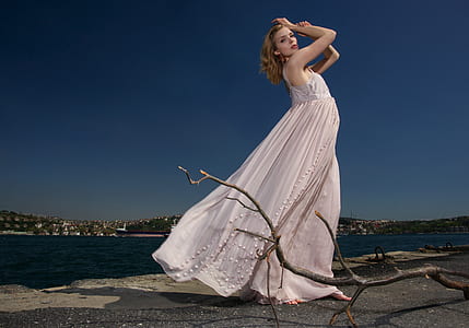woman in white sleeveless dress standing behind body of water during daytime thumbnail