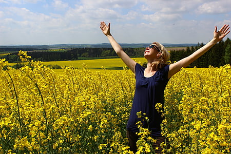 woman in blue scoop-neck dress smiling while looking in sky besides yellow petaled flower field during daytime thumbnail