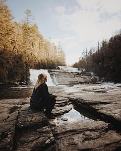 woman sitting on rock facing waterfalls thumbnail