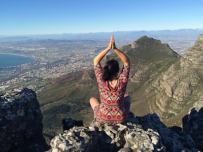 woman sitting on rock cliff facing mountains and plains under blue sky at daytime thumbnail