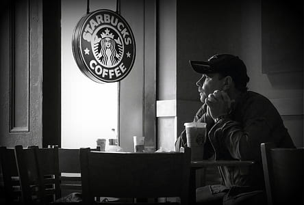 grayscale photo of man sitting at table near Starbucks poster thumbnail
