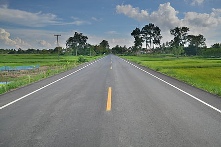 gray asphalt road between green grass field at daytime thumbnail