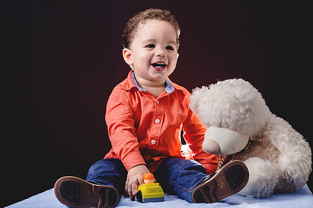 child sitting beside bear plush toy thumbnail