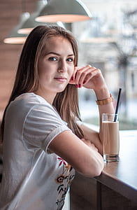 woman in white and multicolored floral t-shirt standing at brown table with chocolate milk selective-focus photography thumbnail