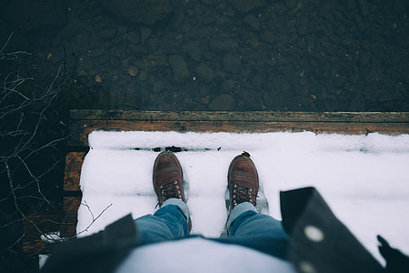 man in blue jeans and white top wearing brown shoes standing on snow thumbnail