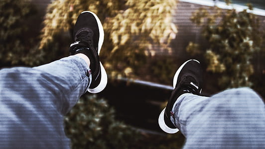 person wearing black-and-white Nike LeBron shoes and blue denim jeans sitting on high ground while feet are hanging on air during daytime thumbnail