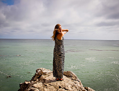 woman in black and white maxi dress on cliff near a sea during daytime thumbnail