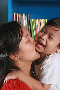 woman kissing boy on chin beside blue wooden bookshelf thumbnail