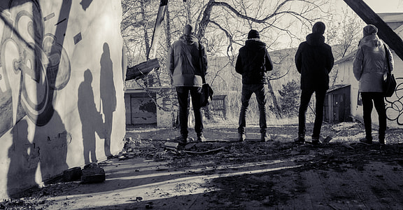 grayscale photo of four men standing near wall facing trees thumbnail