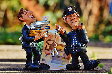 man holding stock of books near policeman holding handcuffs near 50 Euro figurine thumbnail