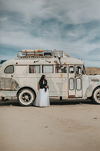 woman in white dress wearing black leather jacket standing beside RV thumbnail