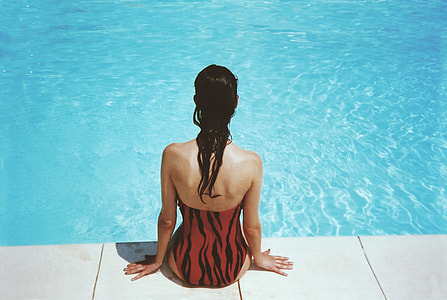 woman wearing red and black monokini sitting on swimming pool during daytime thumbnail