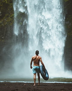 man holding swim ring walking towards waterfalls thumbnail