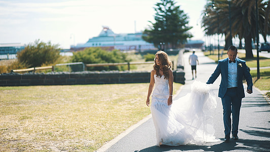 woman in white gown walking along with man in black thumbnail