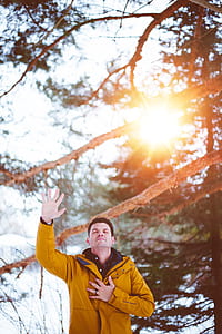 man raising right hand beside tree during daytime thumbnail