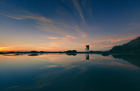 silhouette photography of person standing beside body of water thumbnail