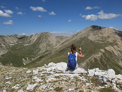 woman with blue backpack sitting on rock facing moutains thumbnail