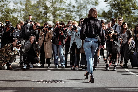 group of people taking picture of woman walking towards them on asphalt road thumbnail