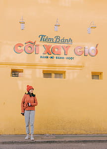 Woman in Orange Sweater and Gray Pants Outfit Standing Near Tiem Banh Wall thumbnail