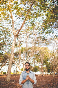 man in blue chambray top standing near green leafed tree thumbnail