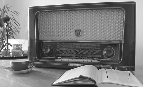 grayscale photography of transistor radio on table near opened book and eyeglasses thumbnail