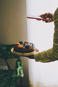 person holding round white and brown icing-covered cake using iPhone thumbnail