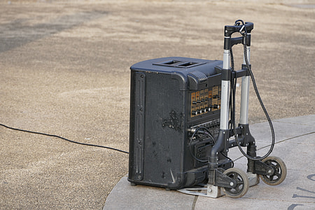black PA monitor speaker on gray folding hand truck on concrete pavement during daytime thumbnail