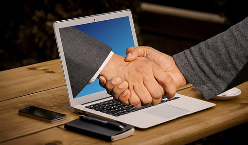 shaking hands near gray laptop computer thumbnail