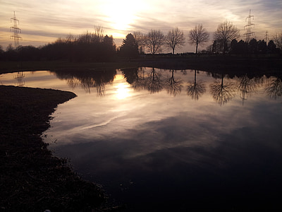 body of water with bare trees beside under yellow sky thumbnail
