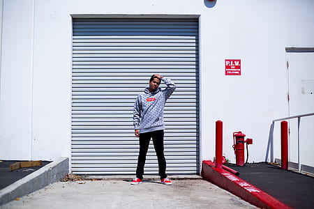 man wearing hooded jacket standing near closed security gate during daytime thumbnail