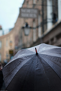 person holding black umbrella near brown concrete building during daytime thumbnail