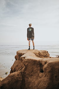 man standing on brown rock cliff at daytime thumbnail