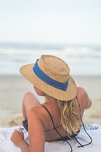 selective focus photography of woman lying on seashore wearing brown hat at daytime thumbnail