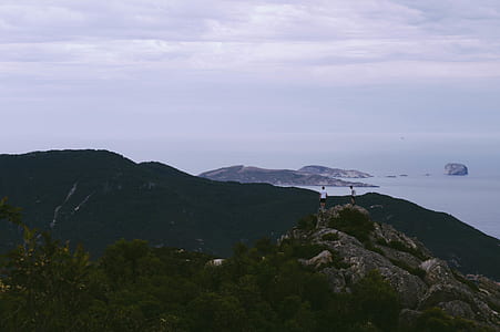 two men on peak of stone mountain near body of water thumbnail