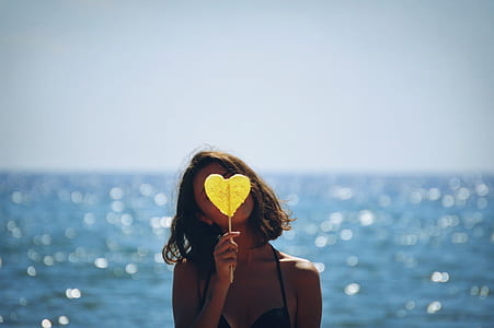 selective focus photography of woman holding yellow heart against sea shore thumbnail
