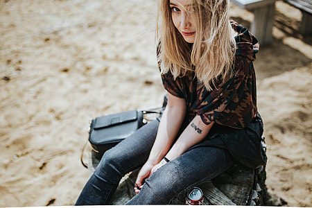 Beautiful blonde woman relaxing with a can of coke on a tree stump by the beach thumbnail