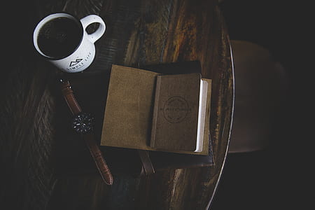brown book near white ceramic mug and round black analog watch placed on brown wooden table thumbnail