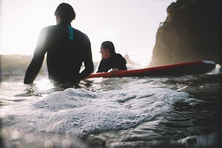 man and woman sitting on seashore holding red surfboard during daytime thumbnail